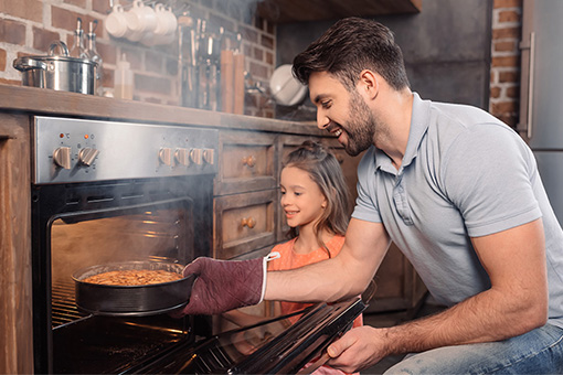 Instalação de gás - Pai e filha em frente ao forno a gás retirando um bolo redondo